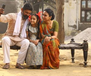 Happy Indian Rural family of Mother, father and daughter sitting together smiling on cot outside their home in front yard using mobile phone. Mother in beautiful saree. Indian culture, traditional. Rural lifestyle.